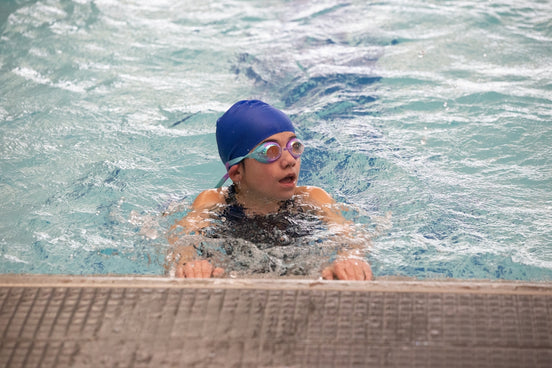 a young boy wearing a swimming cap and goggles in a swimming pool