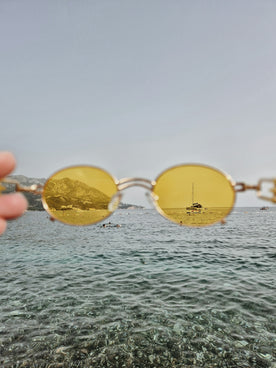 A person holding a pair of yellow sunglasses over a body of water